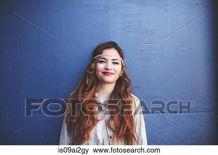 Stock Photo - Portrait of young woman leaning against blue wall. Fotosearch