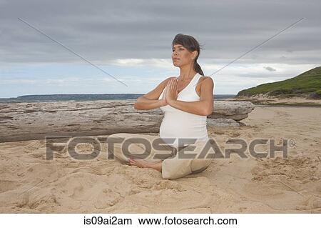 Picture - Pregnant mid adult woman practicing yoga on beach. Fotosearch