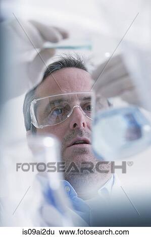 Stock Photograph - Scientist pouring liquid into measuring beaker. Fotosearch