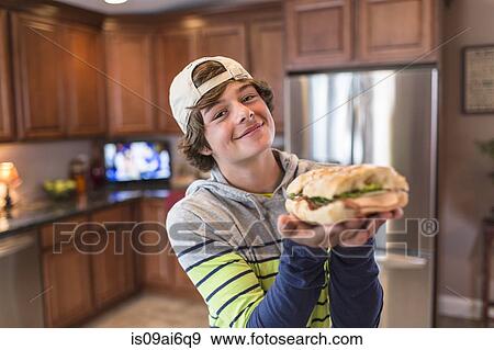 Teenage boy in kitchen holding sandwich View Large Photo Image Stock Photo - Teenage boy in kitchen holding sandwich. Fotosearch