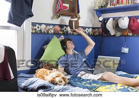Teenage boy lying on bed with laptop computer, football and dog View Large Photo Image Stock Photo - Teenage boy lying on bed with laptop computer, football and dog. Fotosearch
