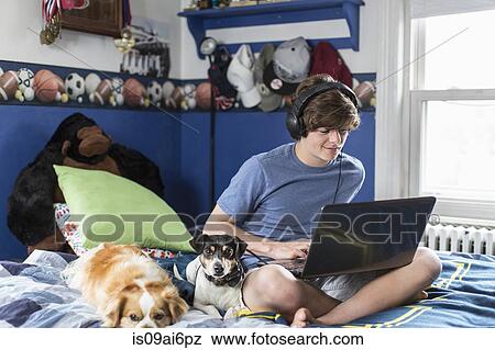 Teenage boy sitting on bed using laptop computer, with dogs View Large Photo Image Stock Photo - Teenage boy sitting on bed using laptop computer, with dogs. Fotosearch