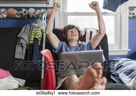 Teenage boy sitting on chair using laptop computer, arms raised View Large Photo Image Stock Image - Teenage boy sitting on chair using laptop computer, arms raised. Fotosearch