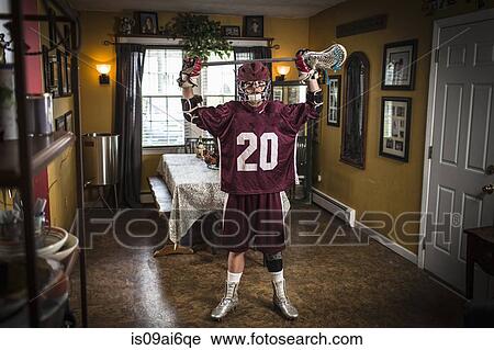 Stock Image - Teenage boy wearing lacrosse uniform, standing in dining room. Fotosearch