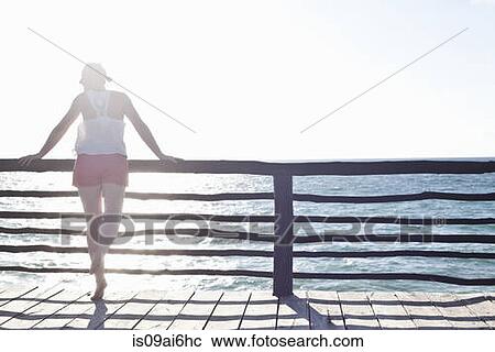 Stock Image - Woman leaning on fence, looking out to sea in Tulum, Mexico. Fotosearch