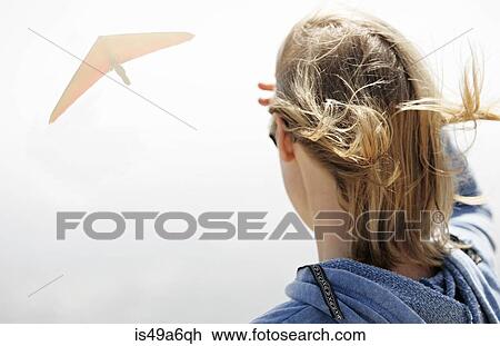 Stock Image - Woman watching hang glider in sky. Fotosearch