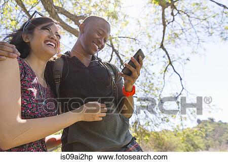 Stock Photography - Young couple in park checking text messages. Fotosearch