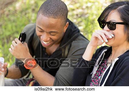 Stock Image - Young couple sitting in park laughing. Fotosearch