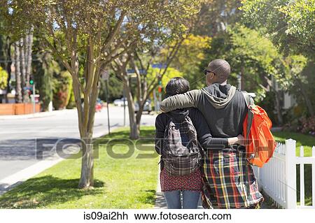 Young couple strolling along sunlit street View Large Photo Image Stock Image - Young couple strolling along sunlit street. Fotosearch
