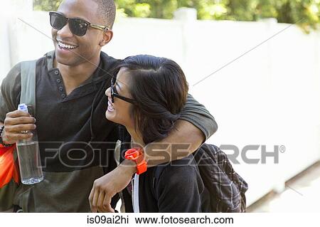 Stock Image - Young couple strolling along sunlit sidewalk. Fotosearch