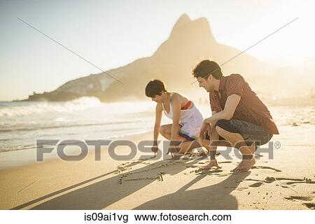 Stock Image - Young couple writing on sand, Ipanema Beach, Rio, Brazil. Fotosearch