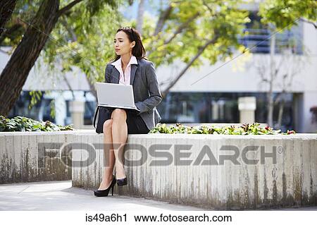Stock Image - Young female businesswoman using laptop outside office. Fotosearch
