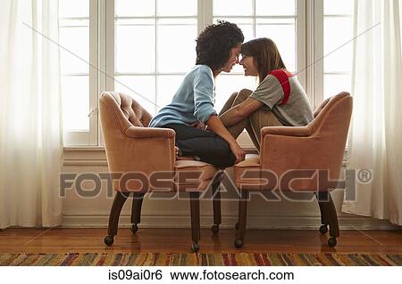 Young female couple sitting head to head in opposite armchairs View Large Photo Image Stock Photograph - Young female couple sitting head to head in opposite armchairs. Fotosearch