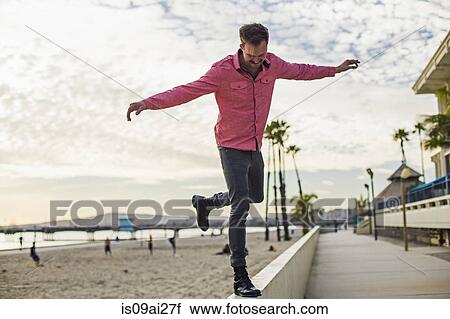 Stock Image - Young man balancing on wall, Long Beach, California, USA. Fotosearch