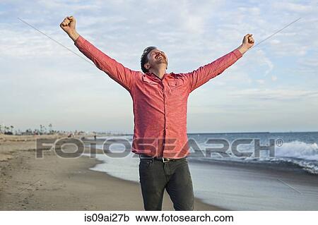 Stock Image - Young man celebrating on beach, Long Beach, California, USA. Fotosearch