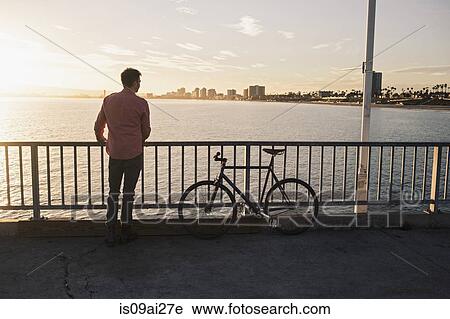 Stock Image - Young man gazing from pier, Long Beach, California, USA. Fotosearch