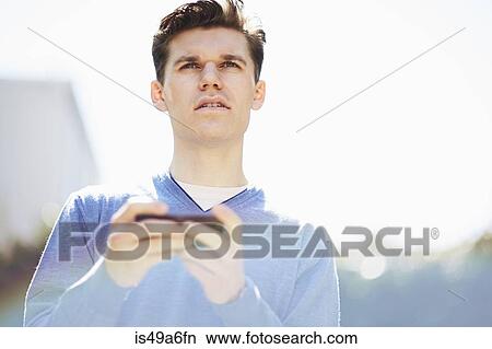 Picture - Young man using smartphone, looking away. Fotosearch