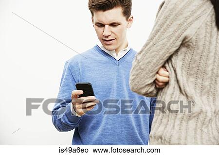 Young man using smartphone, woman in foreground View Large Photo Image Picture - Young man using smartphone, woman in foreground. Fotosearch