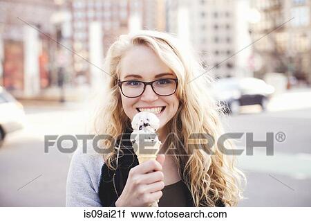 Stock Image - Young woman eating ice cream in street. Fotosearch
