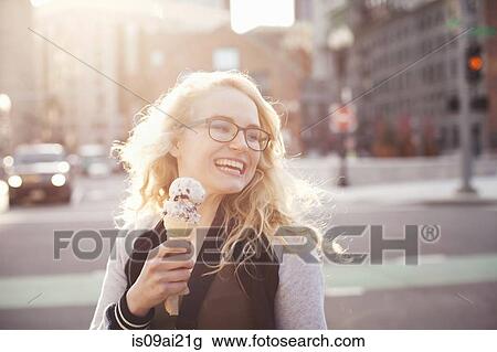 Stock Image - Young woman eating ice cream in street. Fotosearch
