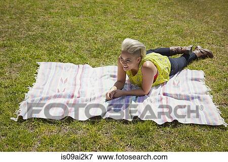 Stock Photo - Young woman lying on rug on park grass. Fotosearch