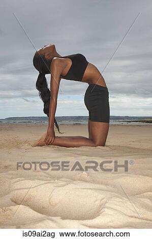 Stock Image - Young woman practicing yoga on beach. Fotosearch