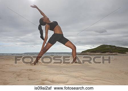 Stock Image - Young woman practicing yoga position on beach. Fotosearch