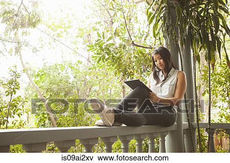 Young woman using digital tablet on porch View Large Photo Image Stock Photo - Young woman using digital tablet on porch. Fotosearch