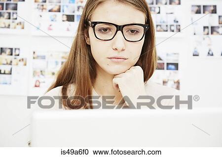 Stock Image - Young woman wearing glasses using computer. Fotosearch