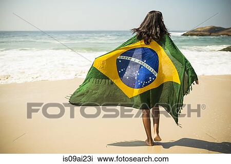 Stock Image - Young woman wrapped in Brazilian flag, Arpoador beach, Rio De Janeiro, Brazil. Fotosearch