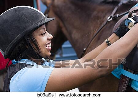 Close up of young woman putting saddle on horse View Large Photo Image Stock Image - Close up of young woman putting saddle on horse. Fotosearch