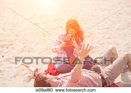 Stock Image - Couple having fun with instant camera on beach. Fotosearch
