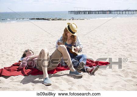 Couple sunbathing and playing ukulele on beach View Large Photo Image Stock Photo - Couple sunbathing and playing ukulele on beach. Fotosearch