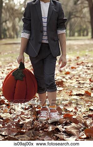 Stock Photo - Cropped image of boy in forest holding pumpkin head. Fotosearch