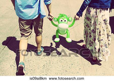 Picture - Cropped rear view of couple holding hands with inflatable monkey. Fotosearch