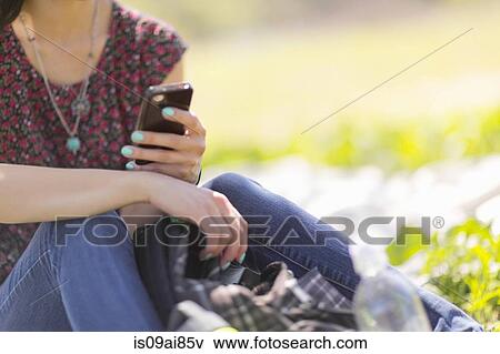 Cropped shot of young woman sitting in park with smartphone View Large Photo Image Stock Photo - Cropped shot of young woman sitting in park with smartphone. Fotosearch