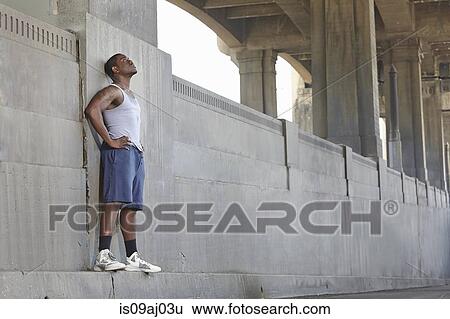 Exhausted young male runner leaning against city bridge View Large Photo Image Stock Photograph - Exhausted young male runner leaning against city bridge. Fotosearch