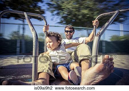 Stock Image - Father and toddler daughter spinning on park roundabout. Fotosearch