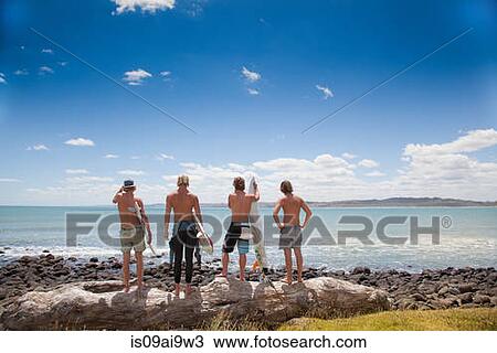 Four young male surfer friends watching sea from rocks View Large Photo Image Stock Image - Four young male surfer friends watching sea from rocks. Fotosearch