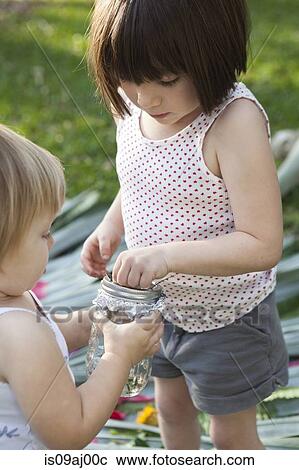 Stock Image - Girl and toddler sister holding jar with green anole lizard in garden. Fotosearch