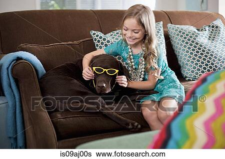 Stock Photograph - Girl holding sunglasses on reluctant chocolate colored labrador dog. Fotosearch