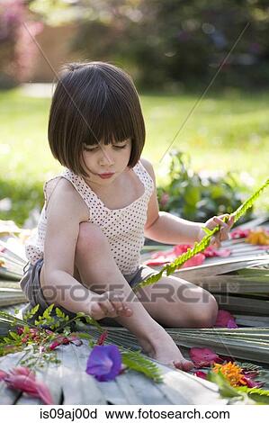 Stock Image - Girl with fern making flower and leaf display in garden. Fotosearch
