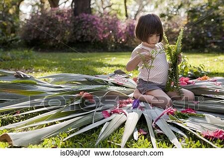 Stock Image - Girl with fern sitting on flower and leaf display in garden. Fotosearch