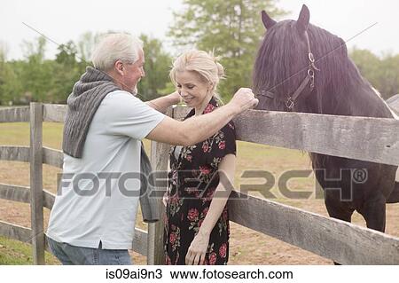 Stock Image - Horse watching mature couple over fence. Fotosearch