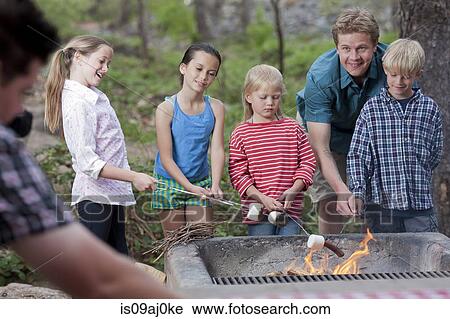 Stock Image - Mature couple and four children toasting marshmallows on campsite, Sedona, Arizona, USA. Fotosearch