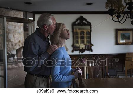 Stock Photograph - Mature couple sharing tender moment in dining room. Fotosearch