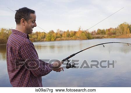 Mature male fisherman reeling in catch from lake View Large Photo Image Stock Image - Mature male fisherman reeling in catch from lake. Fotosearch