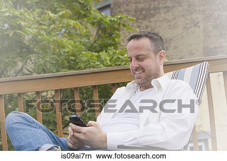 Mature man in garden deck chair texting on smartphone View Large Photo Image Picture - Mature man in garden deck chair texting on smartphone. Fotosearch