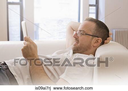 Mature man reclining on sofa looking at digital tablet View Large Photo Image Stock Image - Mature man reclining on sofa looking at digital tablet. Fotosearch