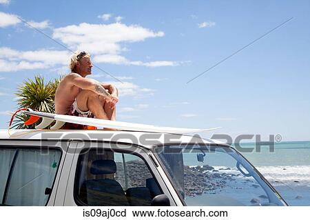 Mature man with surfboard watching from vehicle roof at beach View Large Photo Image Stock Image - Mature man with surfboard watching from vehicle roof at beach. Fotosearch